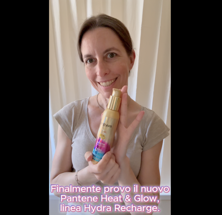 Una donna sorridente tiene in mano il flacone dorato del termoprotettore Pantene Heat & Glow della linea Hydra Recharge. In basso è visibile la scritta con i sottotitoli del video.